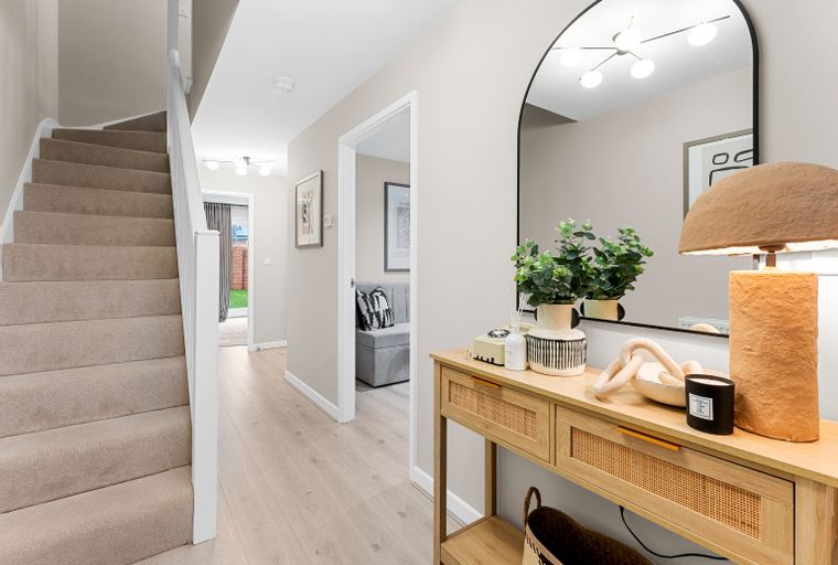 A hallway with a carpeted staircase, a console table, and a mirror.