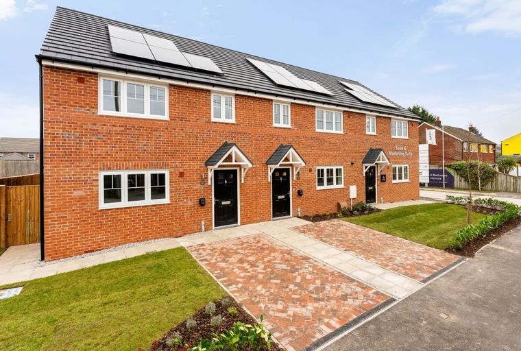 A row of red brick townhouses with black doors, white windows, and solar panels on the roof.