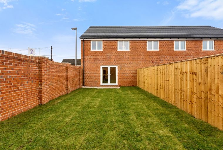 A backyard with a brick house, a brick wall, and a wooden fence.