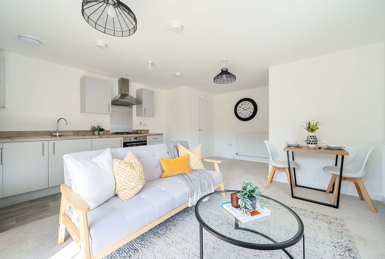 A living room and kitchen area with a sofa, coffee table, dining table, and kitchen cabinets.