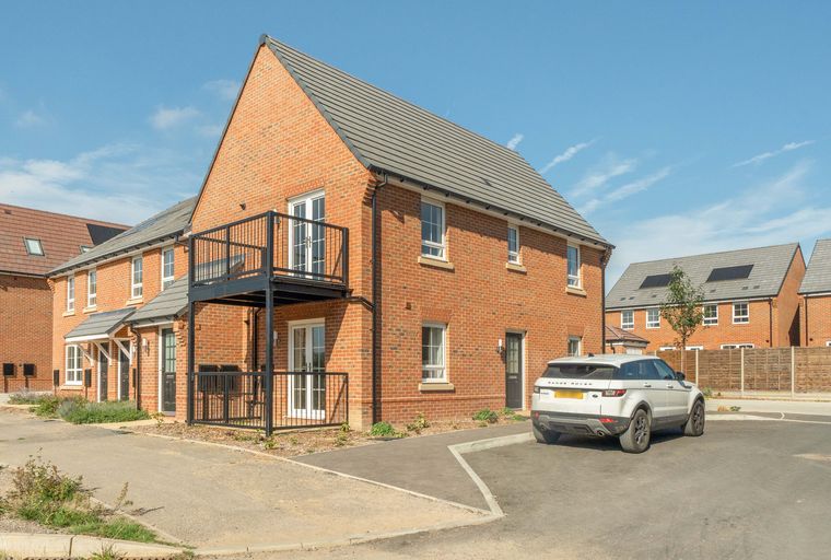 A white Range Rover is parked in front of a brick house with a balcony.