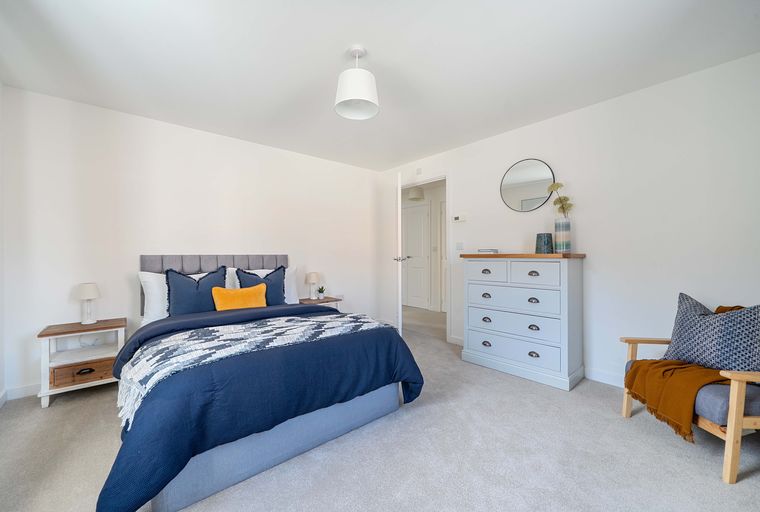 A bedroom with a bed, dresser, and armchair.