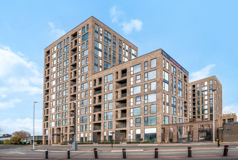 A modern brick apartment building with many windows and balconies under a blue sky with clouds.