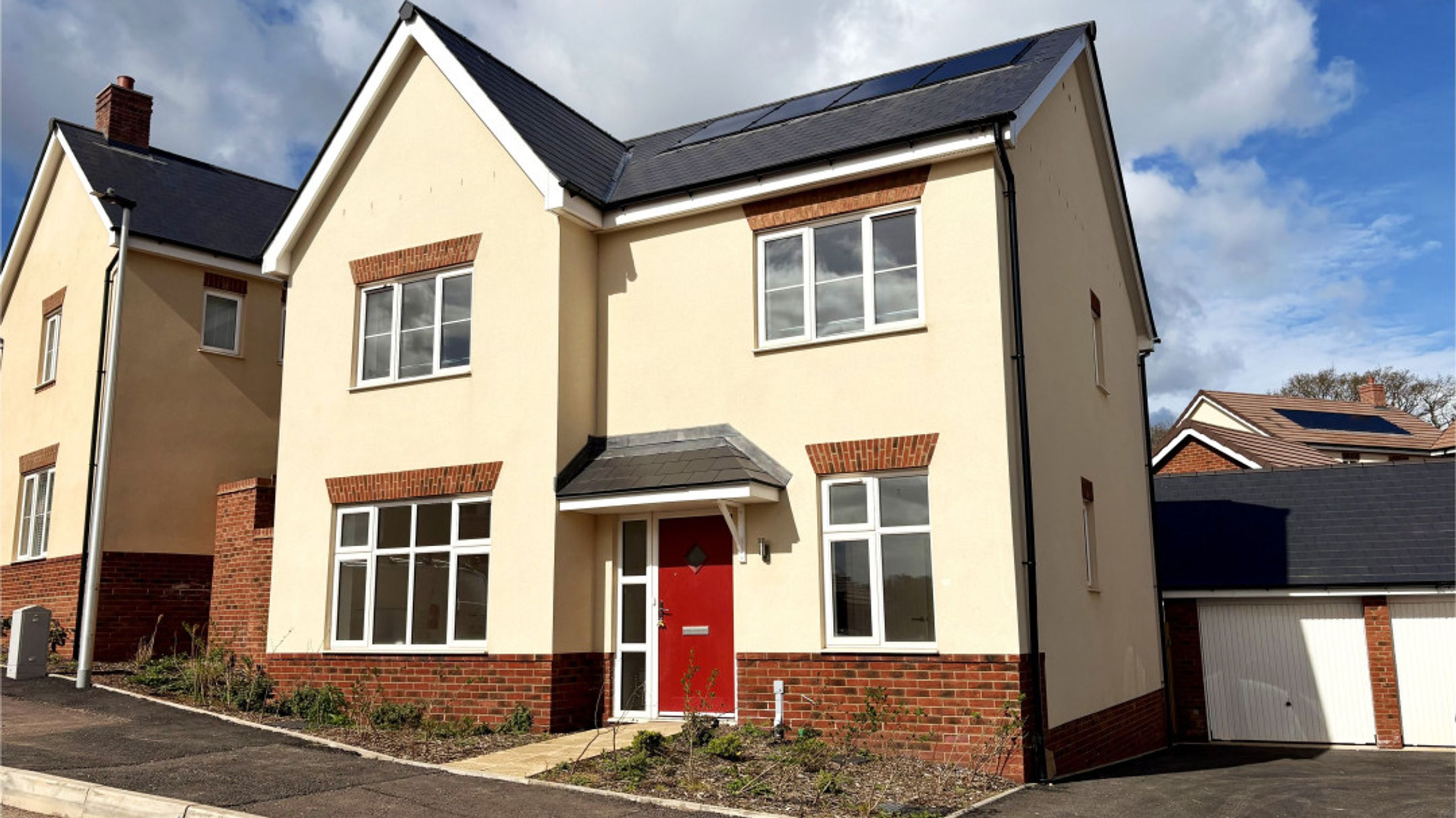 A cream-colored house with a red front door and solar panels on the roof.