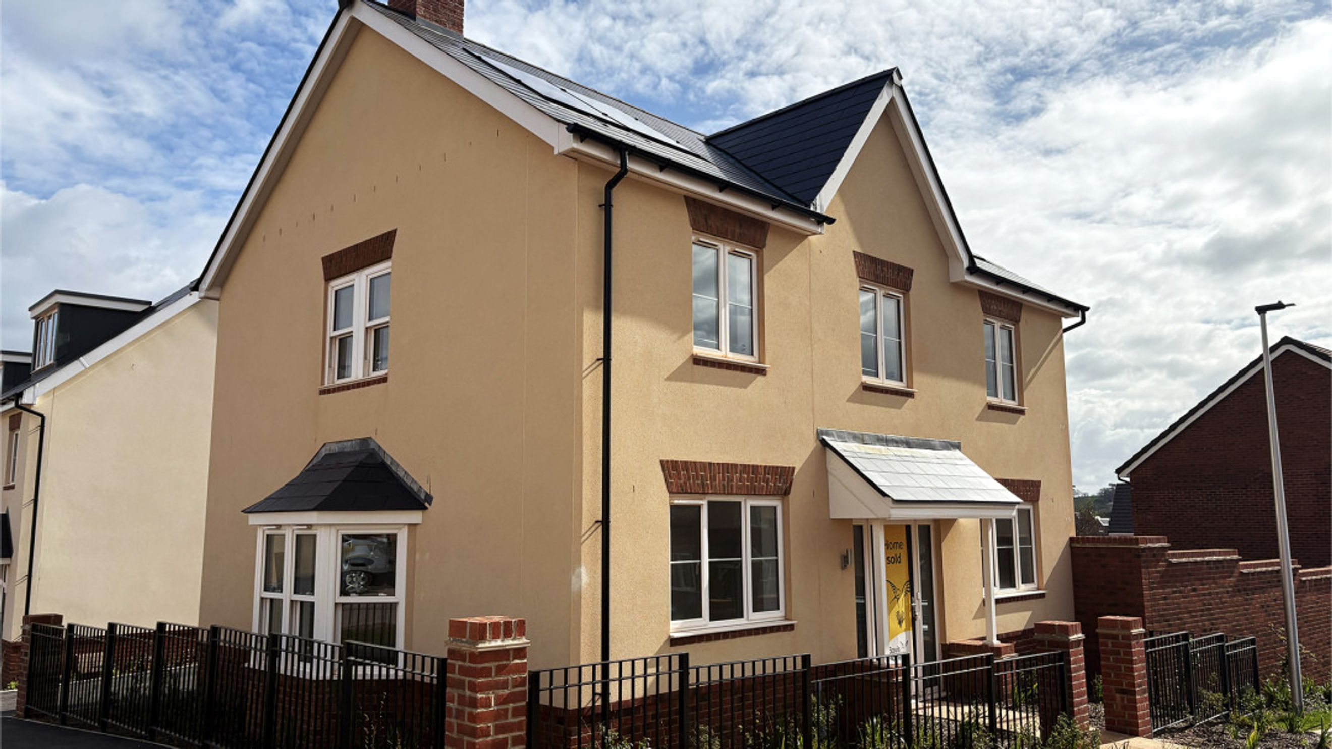A beige stucco house with white windows and a dark tiled roof.