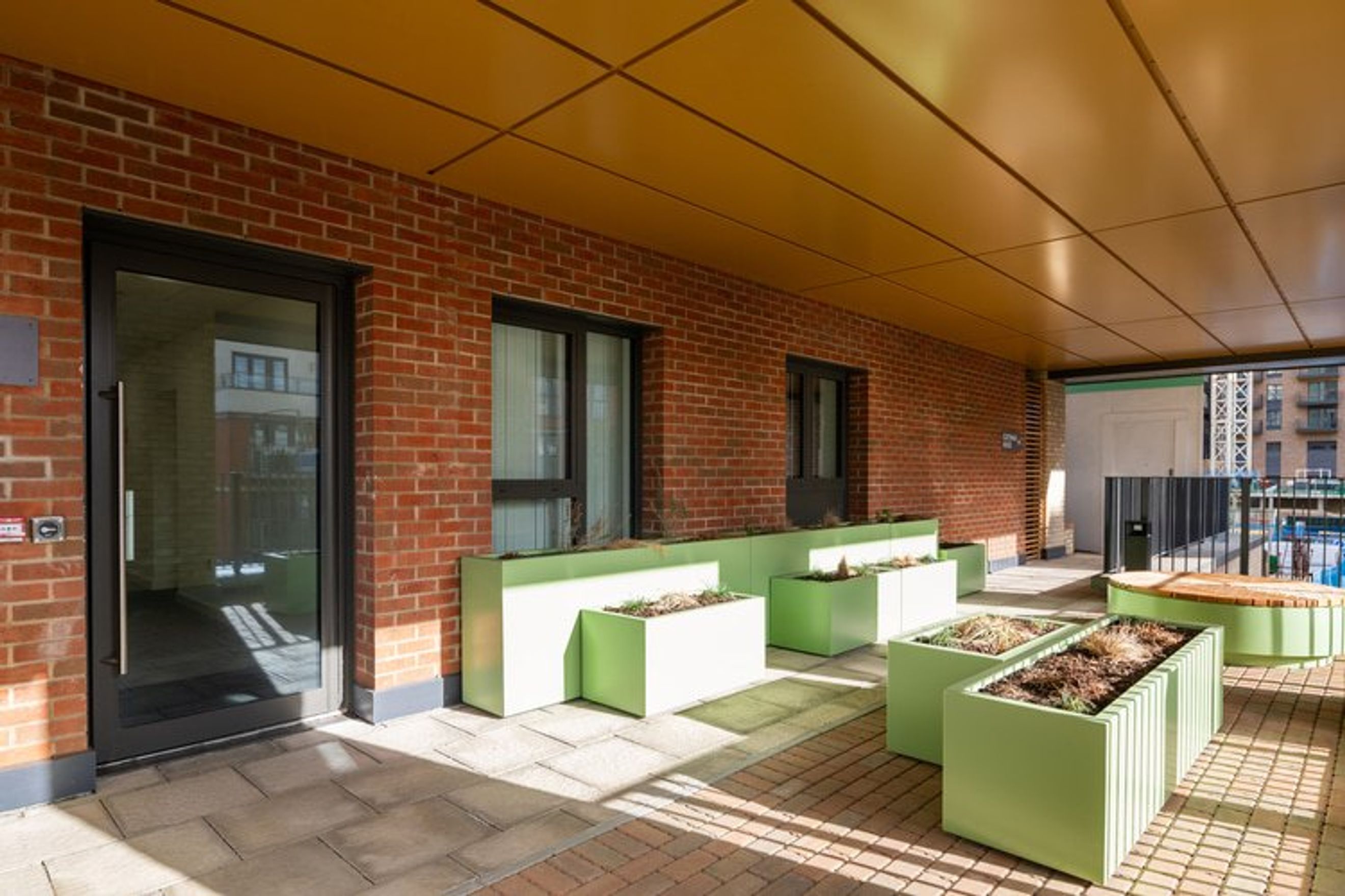 A covered outdoor walkway with brick walls, glass doors, and lime-green planters.