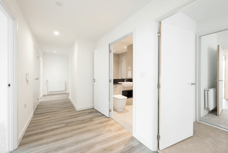 A hallway with doors leading to a bathroom and other rooms, featuring light wood-effect flooring and white walls.