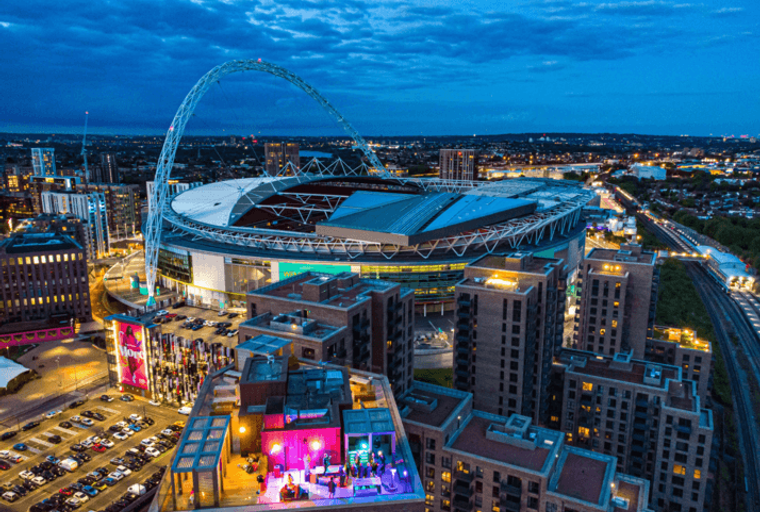 A cityscape at dusk featuring Wembley Stadium and surrounding apartment buildings.