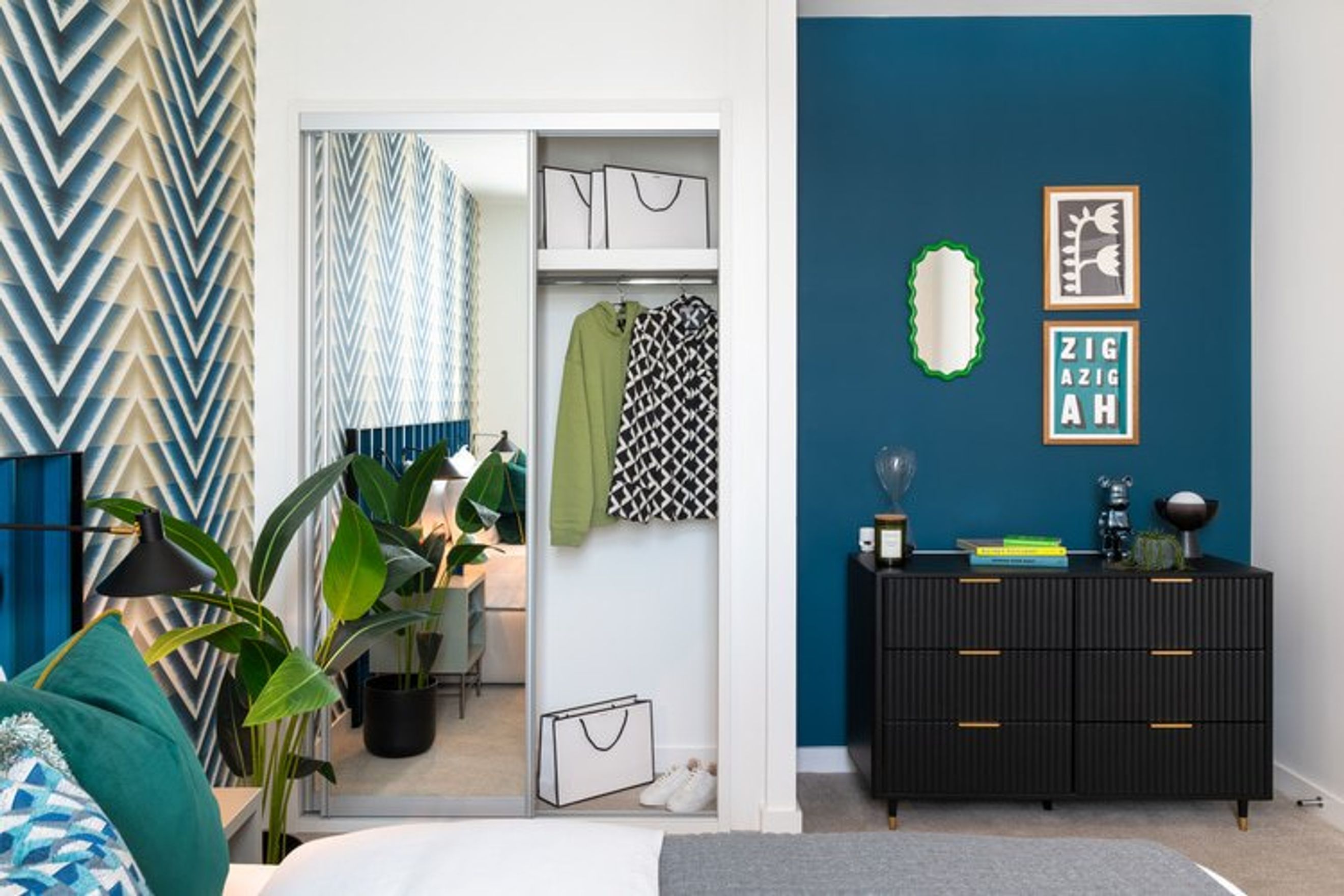 A bedroom with a closet, dresser, and decorative wall art.