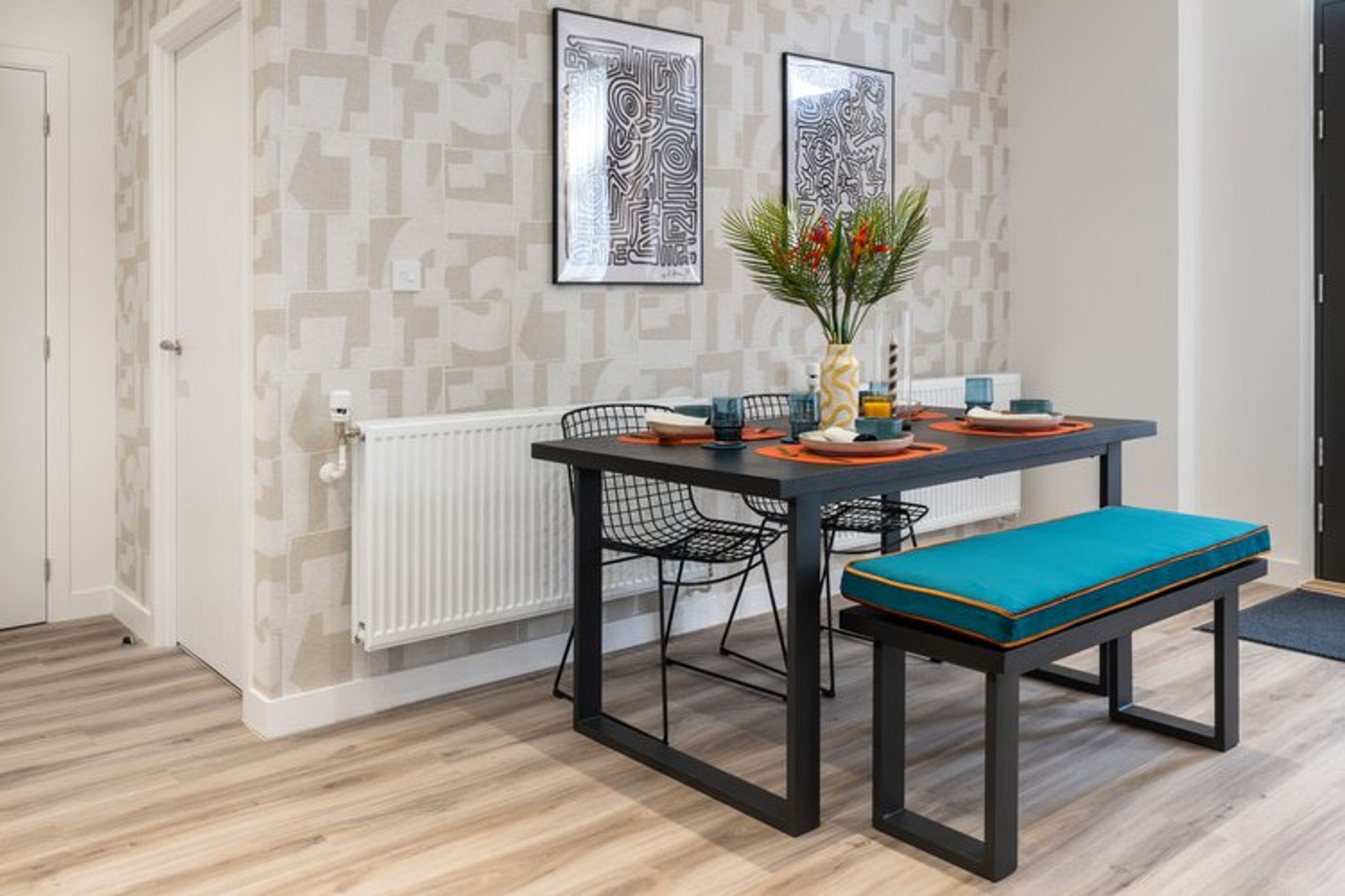 A dining table with chairs and a bench set in a room with patterned wallpaper.