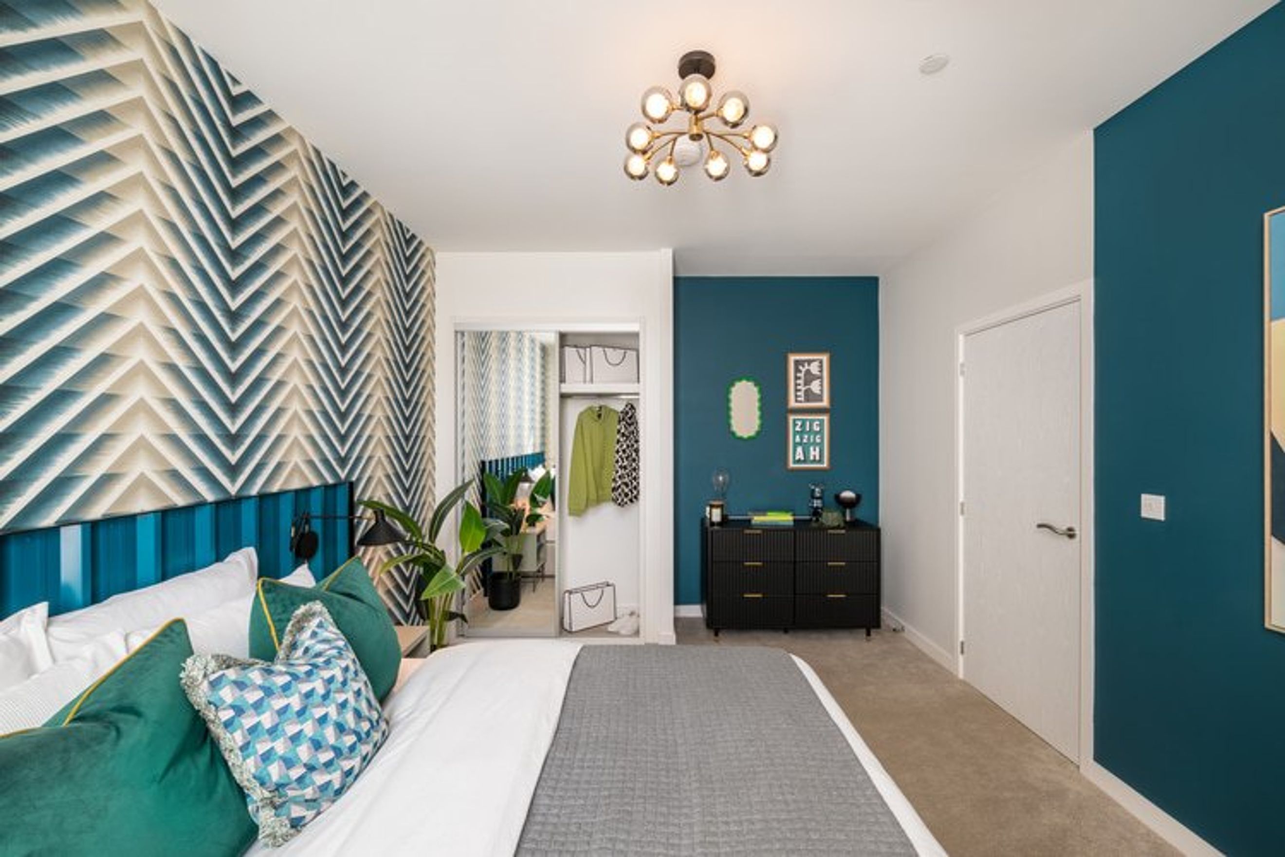 A bedroom with a bed, a dresser, and a geometric accent wall.