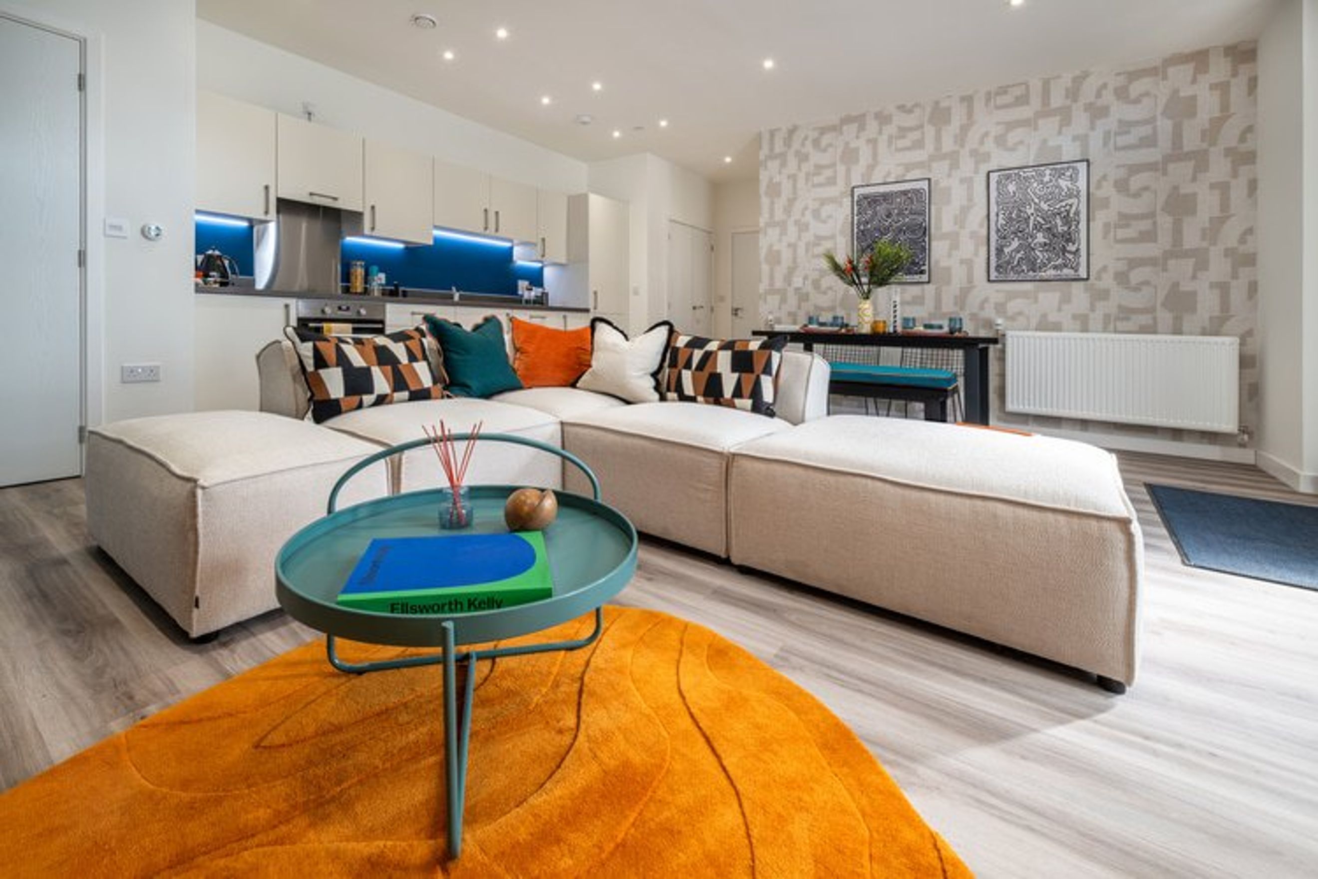 A living room and kitchen area with a sectional sofa, coffee table, and kitchen cabinets.