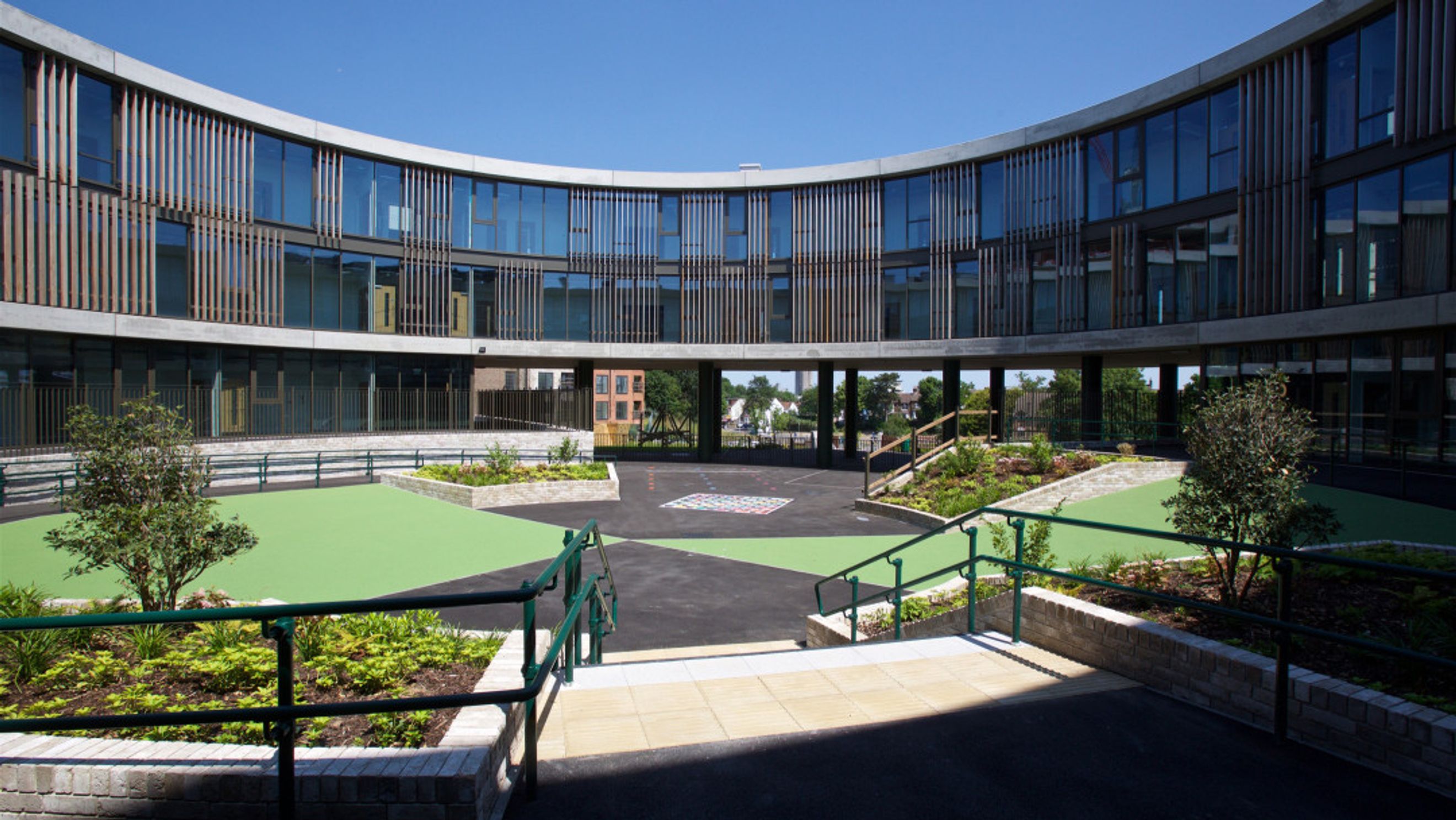 A modern curved building with a courtyard featuring green play areas and landscaping.