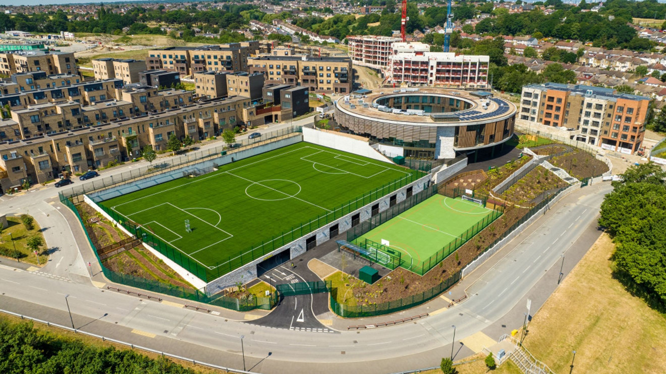 An aerial view of a modern housing development with sports fields and a circular building.