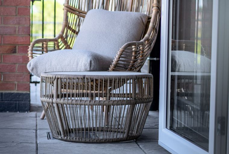A wicker chair and coffee table on a patio next to a brick wall.