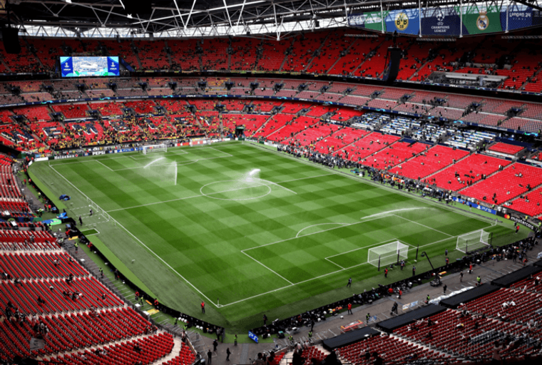 A football stadium with a green pitch and red seats.