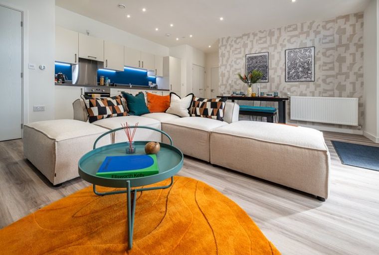 A living room and kitchen area with a sectional sofa, coffee table, and kitchen cabinets.