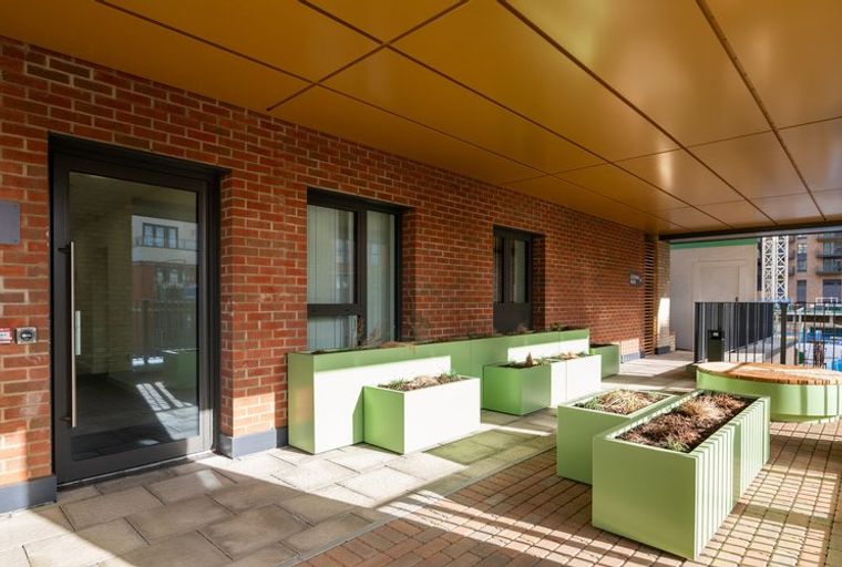 A covered outdoor walkway with brick walls, glass doors, and lime-green planters.