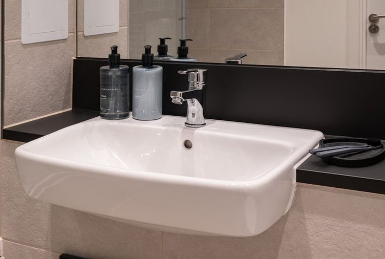 A bathroom sink with two soap dispensers, a faucet, and a toothbrush holder.