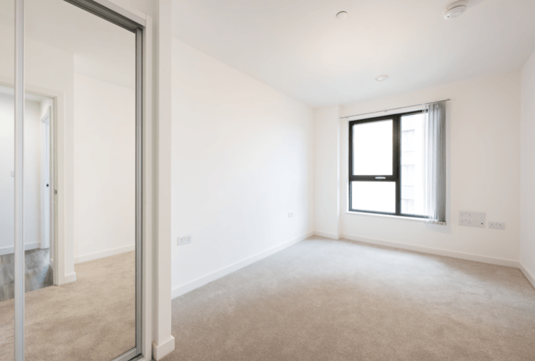 A bedroom with a large window, carpet, and a mirrored wardrobe.