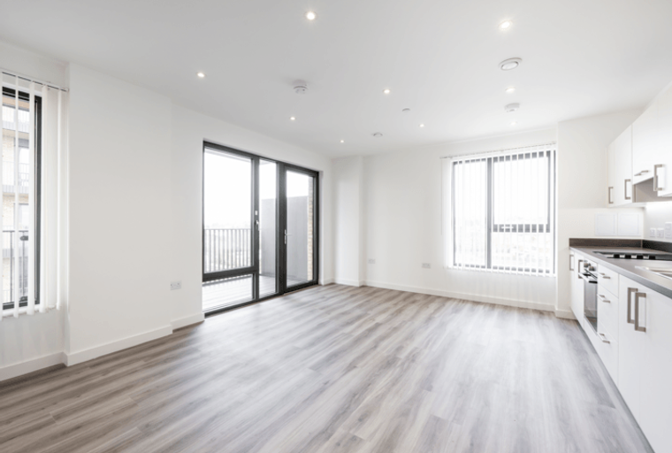 An empty apartment living area with a kitchen and a balcony.