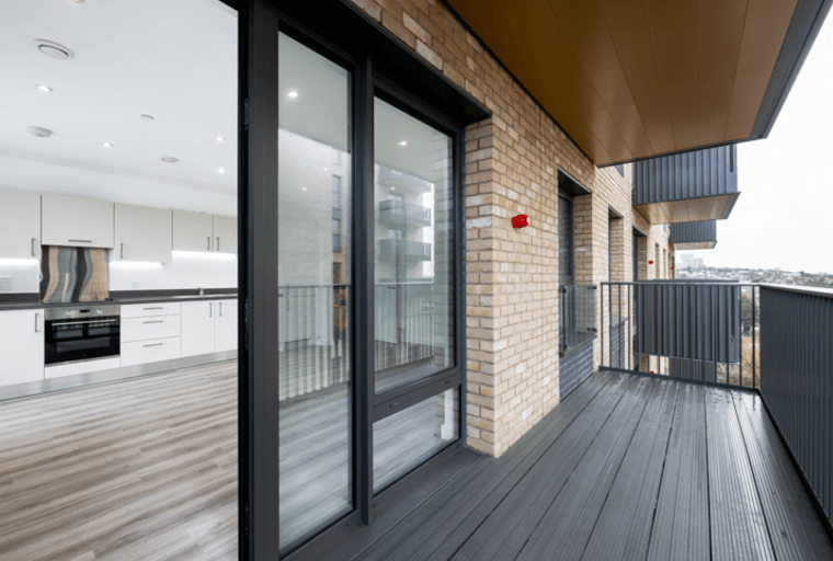 A balcony overlooking a city view, with a modern kitchen visible through sliding glass doors.