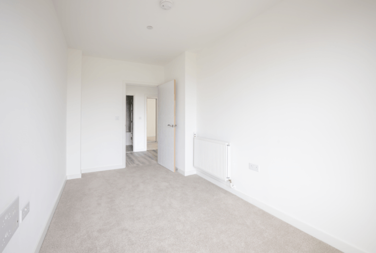 A bedroom with grey carpeting, white walls, and a radiator.