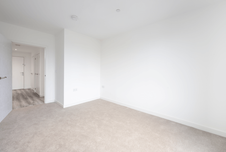 A room with a carpeted floor and white walls, with a doorway leading to a hallway.