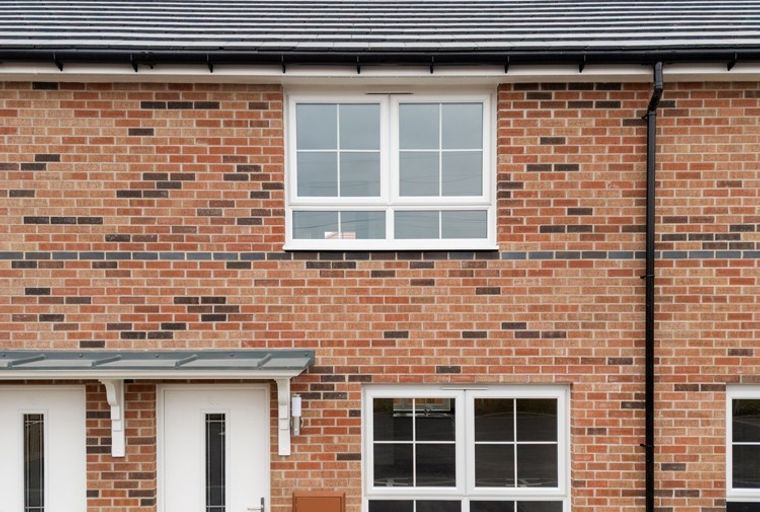 A brick house with white windows and doors under a tiled roof.