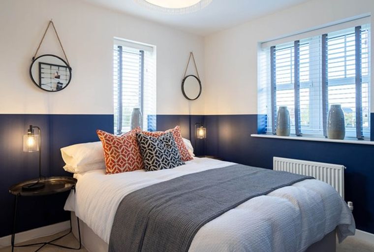 A bedroom with a bed, pillows, a blanket, mirrors, lamps, and windows.