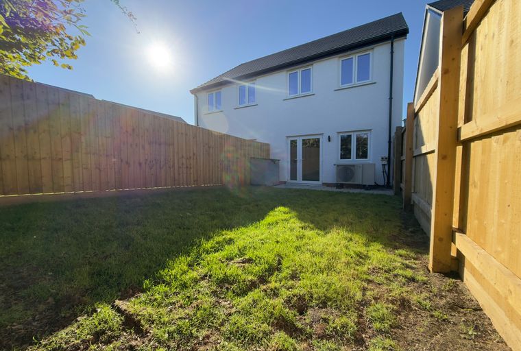 A backyard with a white house, wooden fence, and green grass.