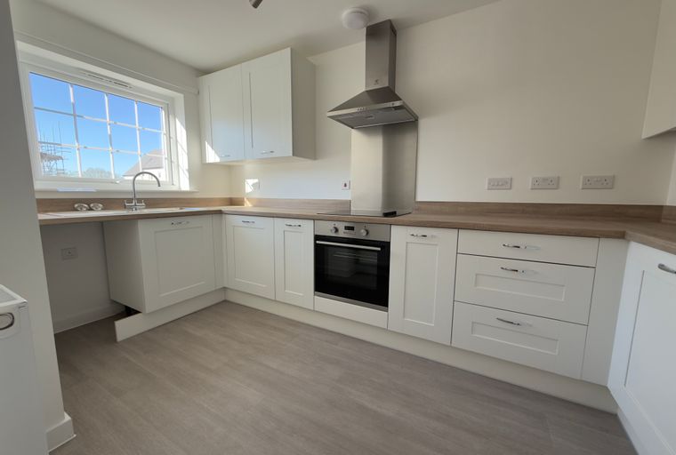A modern kitchen with white cabinets, a built-in oven, and a sink under a window.