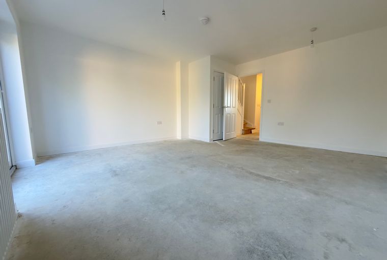 A large, unfinished room with a concrete floor and white walls, featuring an open doorway to a staircase.