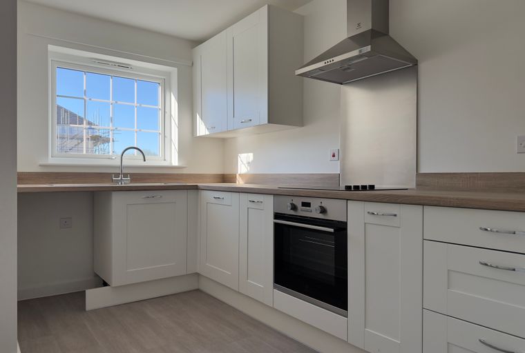 A modern kitchen with white cabinets, a sink, an oven, and a window.