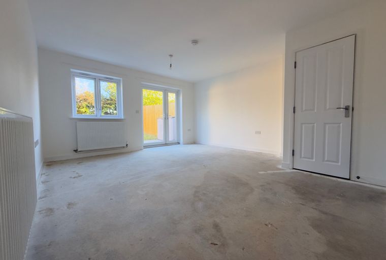 A spacious, unfurnished room with a window, glass doors, and a concrete floor.