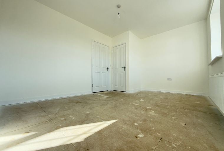 A room with two white doors, a window, and an unfinished floor.
