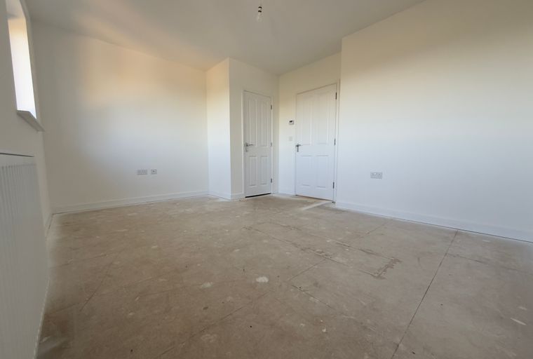 A room with white walls, a concrete floor, and two doors.