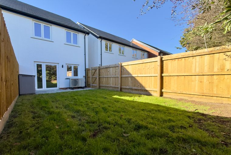 A backyard with a lawn, a wooden fence, and a modern house.