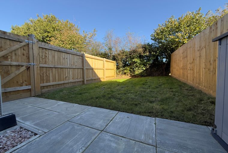 A backyard with a patio, lawn, and wooden fence.