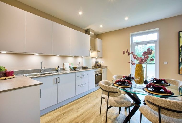 A modern kitchen and dining area with light grey cabinets, a glass-top dining table, and chairs.