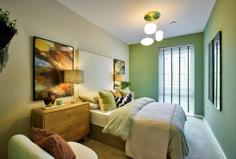 A bedroom with a bed, nightstand, armchair, and abstract art.