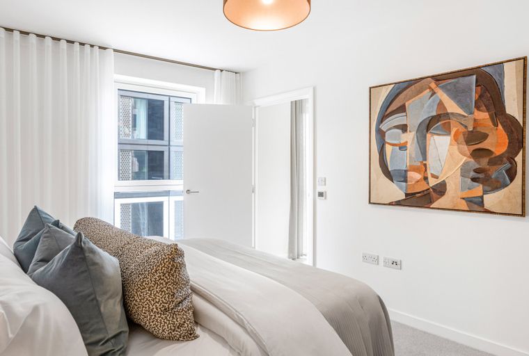 A bedroom with a bed, pillows, abstract art, and a window with curtains.