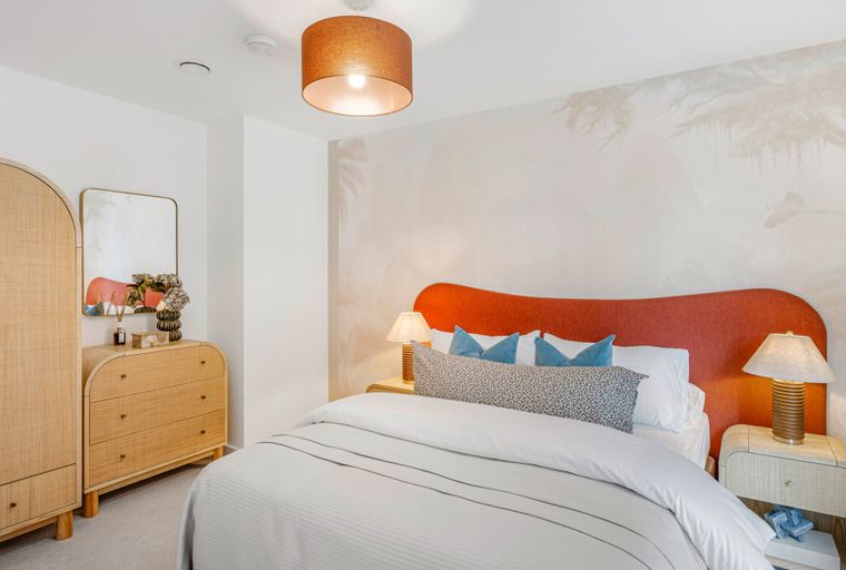 A bedroom with a bed, headboard, bedside tables, lamps, a dresser, and a wardrobe.