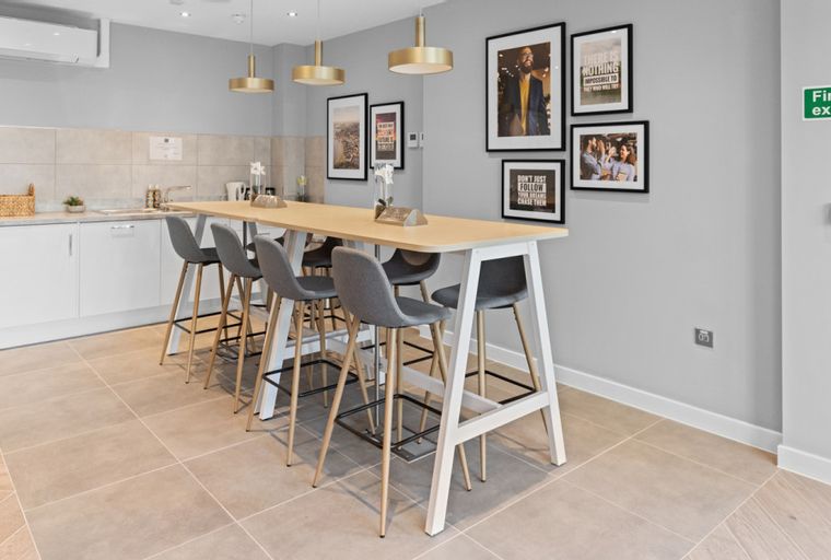 A communal kitchen with a long breakfast bar, stools, and artwork on the wall.