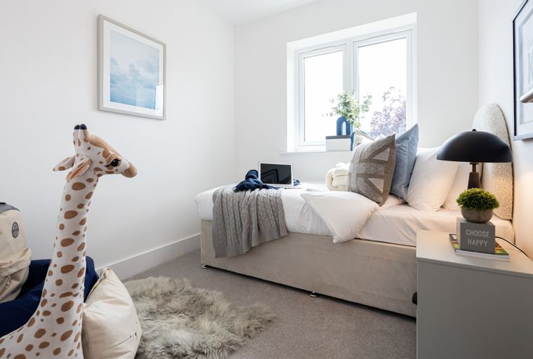 A bedroom with a bed, pillows, a laptop, a stuffed giraffe, and a window.