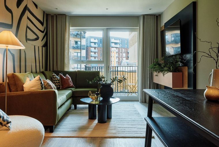 A living room with a green sectional sofa, a coffee table, and a large window overlooking a city view.