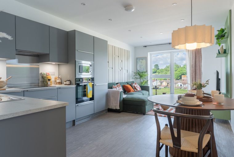 A modern open-plan living space with a grey kitchen, green sofa, and dining table.
