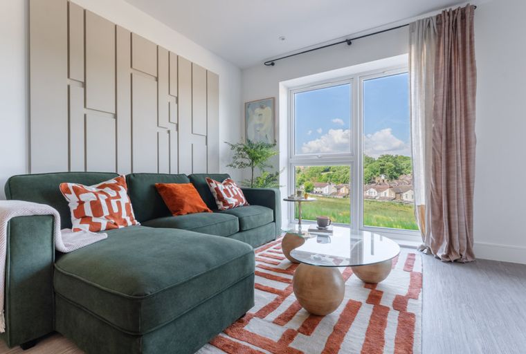 A living room with a green sectional sofa, coffee table, and a large window overlooking a landscape.