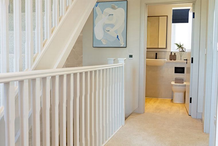 A hallway with a staircase and a doorway leading to a bathroom.