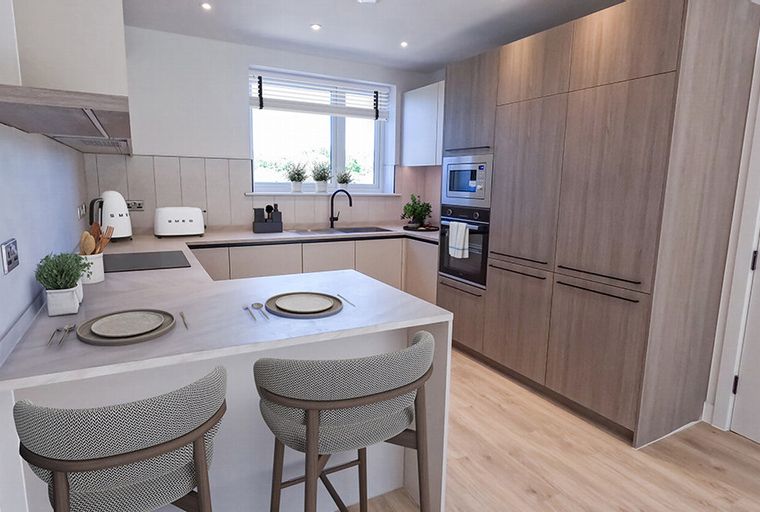 A modern kitchen with light wood cabinets, an island with bar stools, and a window above the sink.
